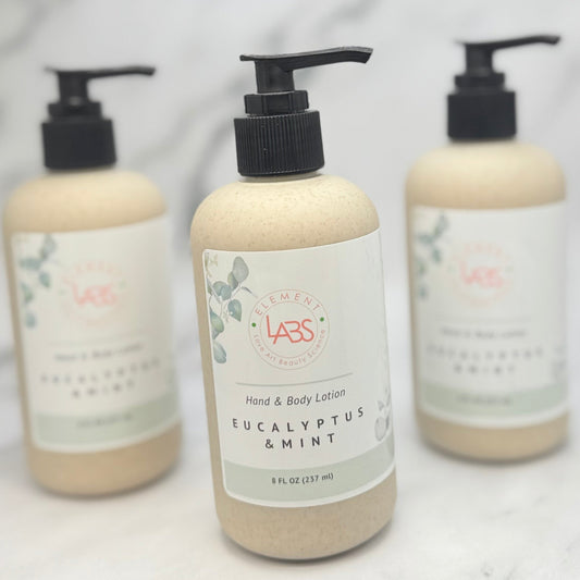 Three pump bottles of LABS Natural Products hand and body lotion in Eucalyptus & Mint, arranged on a light marble surface with the center bottle in sharp focus and the two rear bottles softly blurred.