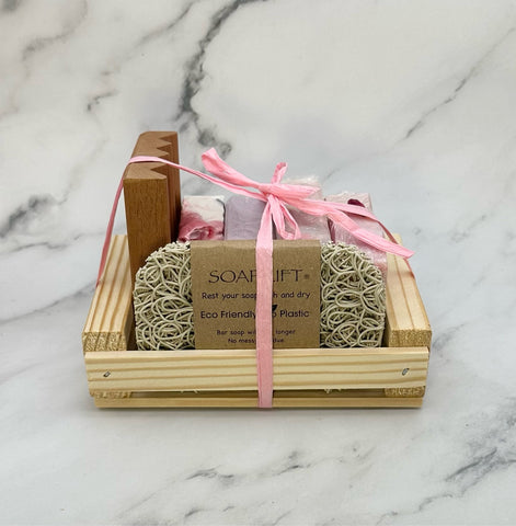 four handcrafted soap bars, a wood soap dish and an eco soap lift displayed in a wood crate tied with a raffia bow. 